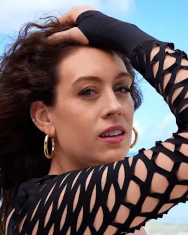 Breanna Stewart stands in front of the bright blue ocean in a black long-sleeve bathing suit with cut-outs.